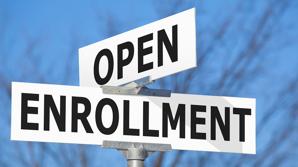 Intersection of white street signs in front of a blue sky that read group open enrollment