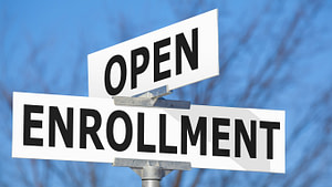 Intersection of white street signs in front of a blue sky that read group open enrollment