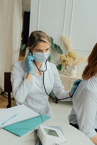 Doctor wearing white lab coat and mask listening to a patient's back with a stethoscope in a procedure covered by a health reimbursement arrangement in Reno, Nevada.