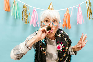 Senior woman in a colorful vest wearing a party hat and blowing into a horn to celebrate the Nevada Birthday Rule for Medicare.