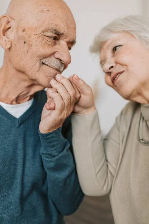 Two older people holding hands and looking at each other learning about Leqembi and Medicare for Alzheimer's treatment.